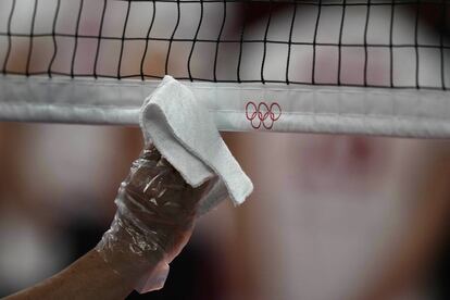 Un operario usa un guante de plástico y un paño para desinfectar la red de voleibol en el Ariake Arena.