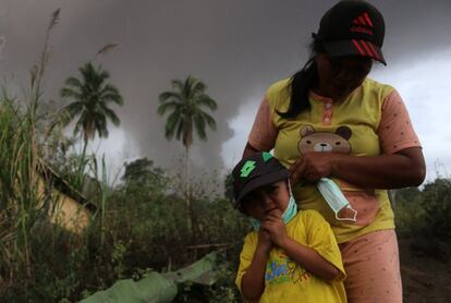 Una mujer coloca una mascarilla a su hija mientras el volcán Sotupan sigue en erupción a sus espaldas en Minahasa, al norte de la isla de Célebes, el 3 de octubre de 2018.  