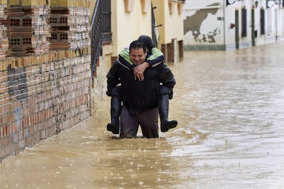 Una persona camina con otra a hombros entre las casas inundadas en la barriada Doña Ana de la localidad de malagueña de Cártama.