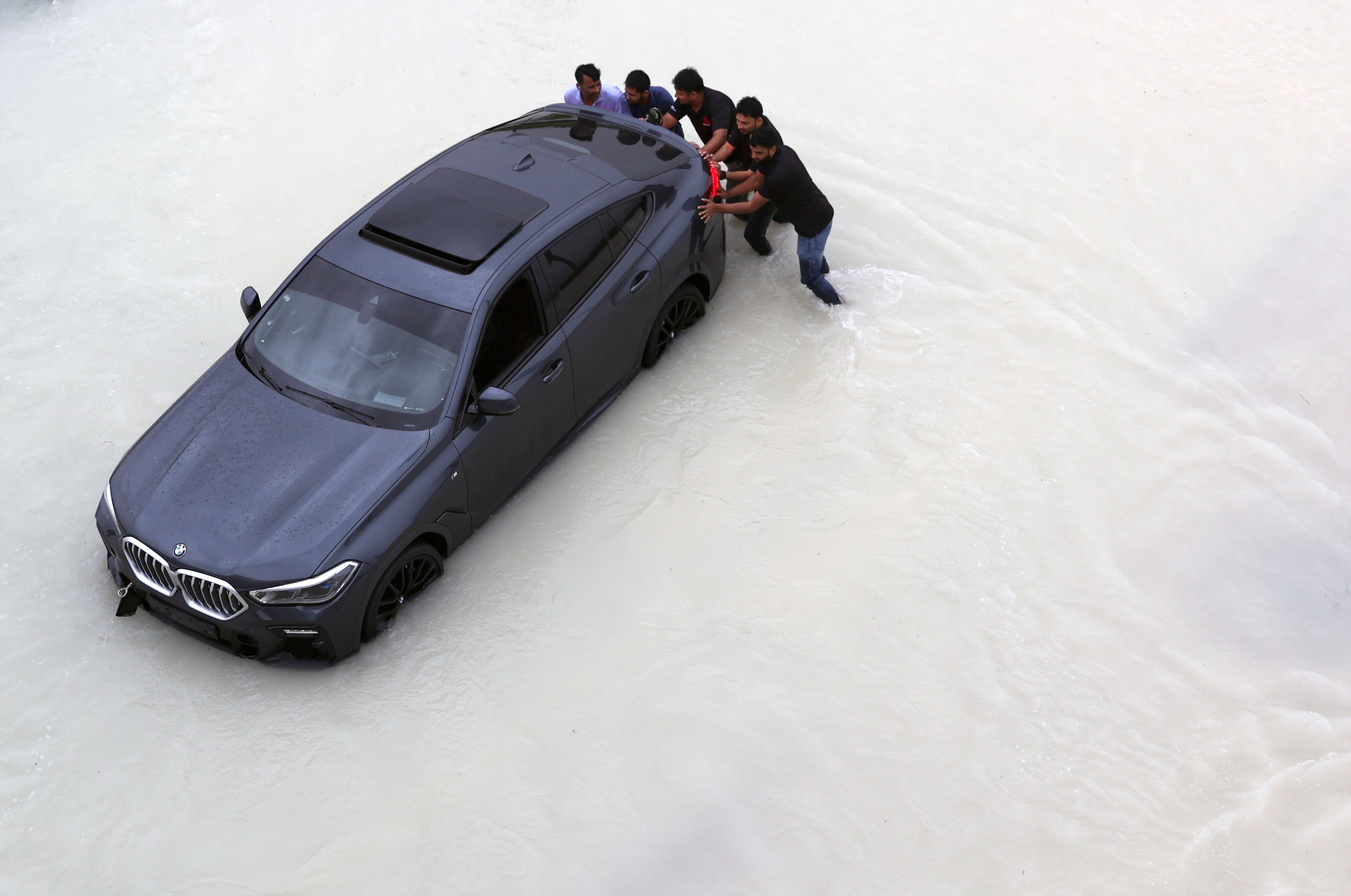 Varias personas empujan en automóvil atrapado por la fuerte lluevía en Dubái, el martes.