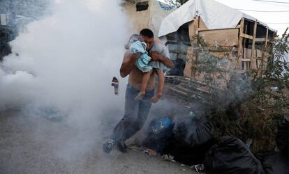 Un hombre escapa con un niño en brazos del gas lacrimógeno lanzado por los antidisturbios el domingo 29 de septiembre en el campo de refugiados de Moria, en la isla griega de Lesbos.