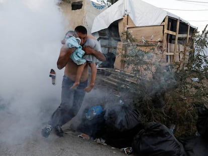 Un hombre escapa con un niño en brazos del gas lacrimógeno lanzado por los antidisturbios el domingo 29 de septiembre en el campo de refugiados de Moria, en la isla griega de Lesbos.