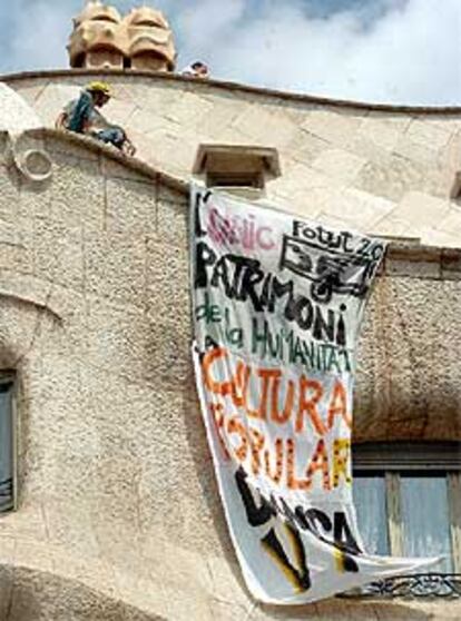 Un joven <i>okupa</i> despliega una pancarta tras acceder al edificio de Gaudí en protesta por el desalojo de Hamsa.
