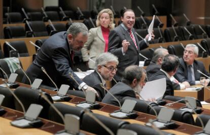 Los diputados Pedro Azpiazu (PNV, de pie), Josep Sánchez Llibre (CiU) y Francisco Fernández Marugán (PSOE) conversan en la Comisión de Economía del Congreso, donde se debate la 'ley Sinde', mientras el diputado del PP, Vicente Martinez Pujalte, en el fondo de la imagen gesticula