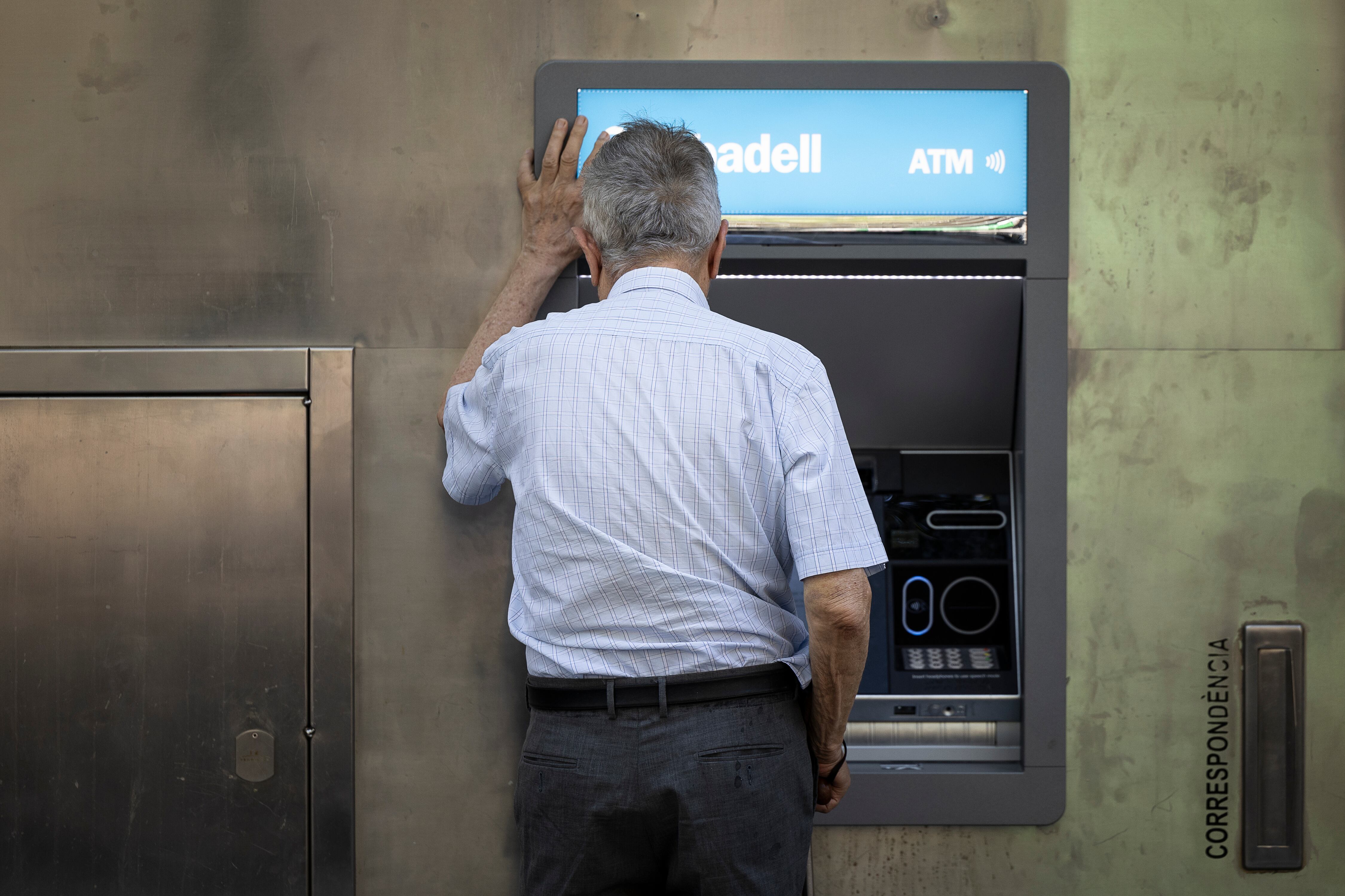 Un anciano saca dinero del cajero en una oficiana del Sabadell.