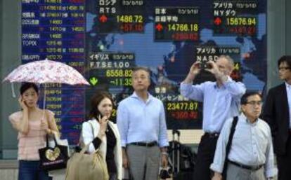 Peatones esperan para cruzar una calle frente a una pantalla con resultados de la Bolsa de Tokio, en Japón. EFE/Archivo