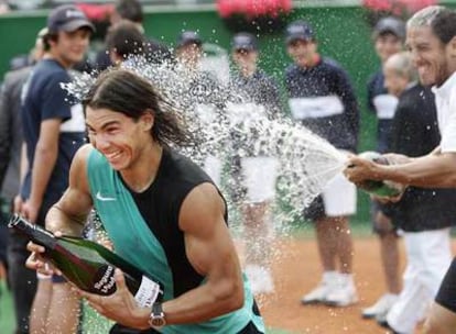 Rafael Nadal, con su propia botella aún sin abrir, trata de esquivar las burbujas de cava que le lanza Guillermo Cañas.
