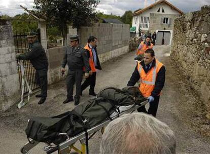 Uno de los cadáveres es trasladado a la ambulancia en presencia de la Guardia Civil. Al fondo, la casa donde residía la pareja.