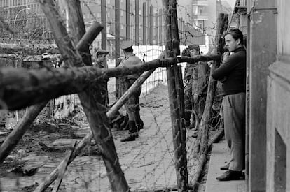 Ciudadanos de Berlín Oeste miran como los soviéticos de Berlín Este construyen el Muro. Los obreros sustituyeron el rollo de alambre de púas, usado para la primera valla provisional, por paneles de hormigón y piedras.