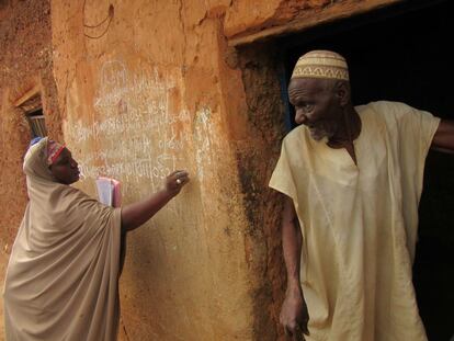El anciano Ahmadu Ahmat se asoma enfadado a la puerta de su casa en Dambatta porque se niega a que vacunen a sus nietos contra la polio mientras la sensibilizadora Zainab Shari escribe en la pared que este domicilio debe ser revisitado.