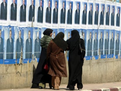 Tres mujeres argelinas pasean junto a un muro lleno de carteles electorales en Argel.