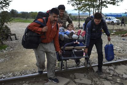 Três homens empurrando um carrinho com um menino e uma menina a bordo cruzam a fronteira entre a Grécia e a Macedônia e caminham até o campo de registro, perto da cidade de Gevgelija, Macedônia, 20 de outubro de 2015.