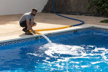 Un operario de una empresa de camiones cisterna rellena varias cubas de agua y la piscina de una urbanización de la localidad de Rincón de la Victoria con la ayuda del jardinero de la comunidad.