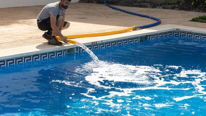 Un operario de una empresa de camiones cisterna rellena varias cubas de agua y la piscina de una urbanización de la localidad de Rincón de la Victoria con la ayuda del jardinero de la comunidad.