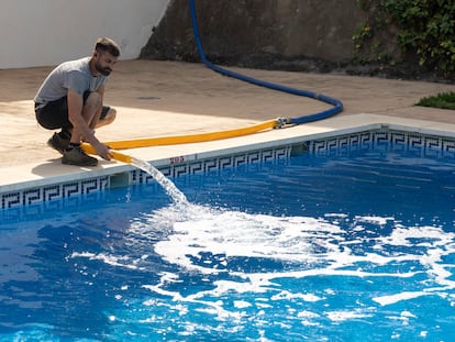 Un operario de una empresa de camiones cisterna rellena varias cubas de agua y la piscina de una urbanización de la localidad de Rincón de la Victoria con la ayuda del jardinero de la comunidad.