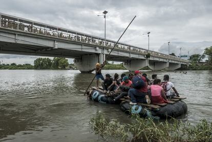 Um grupo de migrantes sobe numa 'câmara', como se chamam as balsas que cruzam o rio Suchiate, sob o olhar de quem espera na ponte.