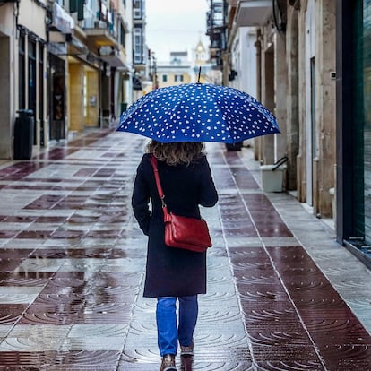 MAHÓN (MENORCA), 07/03/2025.- Una mujer con paraguas se protege de la lluvia este viernes en el carrer Nou del centro histórico de Mahón, Menorca. Este viernes la llegada de una borrasca atlántica prolongará la situación de inestabilidad de los últimos días en Baleares, dejando cielo cubierto con lluvias ocasionales y dispersas, temperaturas estables y viento flojo o moderado del este. EFE/ David Arquimbau Sintes