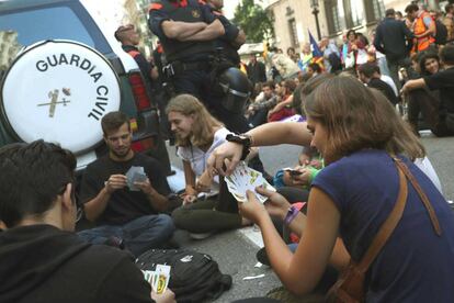 Un grupo de j&oacute;venes juegan a las cartas durante la sentada ante la conseller&iacute;a de Exteriores, en V&iacute;a Laietana, para impedir que el veh&iacute;culo de la Guardia Civil pueda moverse.