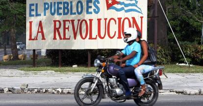 Dos personas pasan en moto delante de un cartel alusivo a la revoluci&oacute;n cubana, ayer en La Habana.