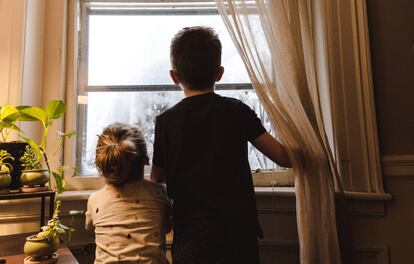 Duas crianças olham por uma janela. Quarentena impõe desafio para pais e filhos.