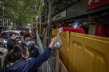 Un vendedor con máscara protectora entrega una bolsa con comida sobre una valla de seguridad en una zona residencial de Wuhan. La ciudad china, origen del brote de coronavirus, terminará este miércoles su confinamiento y permitirá que la población entre y salga de la ciudad.