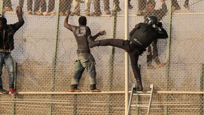 Un agente trata de alcanzar a un inmigrante encaramado en la valla de Melilla.