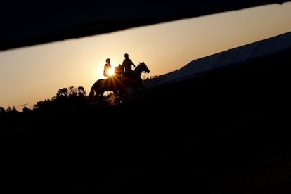 Dos jockeys caminan junto a sus caballos durante una sesión de entrenamientos en el hipódromo Pimlico, en Baltimore, Maryland.