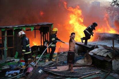 Un joven grita mientras varios bomberos intentan apagar un incendio declarado en Madaluyog, al este de Manila (Filipinas).
