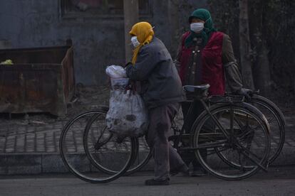 Dos personas con mascarillas circulan con sus bicicletas por las atascadas calles de Qingdao.