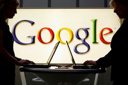 Dos personas usan sus portátiles frente al logo de Google en la feria de Hannover, Alemania, en 2017.