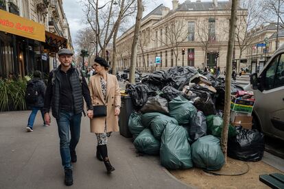 Gente caminando junto a las bolsas de basura que no han sido recogido, este lunes.  Los servicios de limpieza de París están el huelga por la nueva ley de pensiones que pretenden atrasar la jubilación hasta los 64 años.