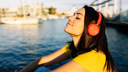 Una mujer con los auriculares puestos escuchando música a la orilla del río.