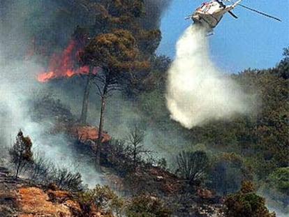 Un helicóptero vierte agua sobre las llamas durante las labores de extinción del incendio junto a la autopista AP-, en Martorell.