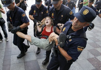 Cuatro agentes de la Policía Nacional llevan en volandas a una joven durante las protestas por el desalojo de Sol. A comienzos de agosto y a dos semanas de la celebración en Madrid de la XXVI Jornada Mundial de la Juventud, y la presencia del papa Benedicto XVI, se desmantela el punto de información que los 'indignados' mantenían en la Puerta del Sol de Madrid en una acción coordinada del Ministerio del Interior y del Ayuntamiento de Madrid. Para evitar nuevas concentraciones, la Delegación del Gobierno ordena cortar totalmente el acceso a la plaza, decisión insólita desde el nacimiento del 15-M, prohibiendo la entrada de 'indignados', periodistas y viandantes. Las medidas reavivaron el movimiento, cuyos integrantes deciden diversificar las protestas por los alrededores.