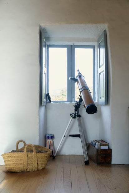 Rincón del salón, con el leñero de esparto, la media fanega de castaño y el telescopio orientado hacia la luna de invierno.