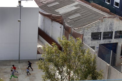 Unos niños corretean en la escuela Els Encants, junto a un edificio con tejado de fibrocemento.