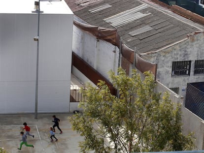 Unos niños corretean en la escuela Els Encants, junto a un edificio con tejado de fibrocemento.