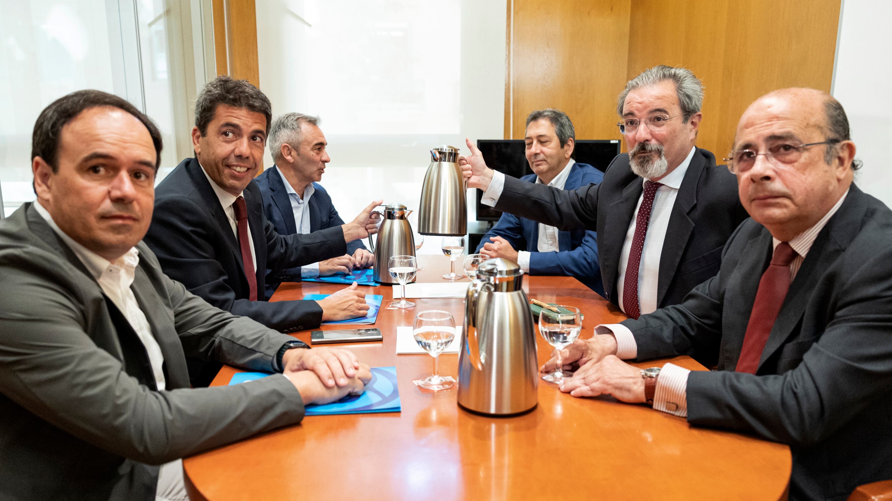 El líder del PP en la Comunidad Valenciana, Carlos Mazón (centro izquierda), acompañada de su equipo, durante la reunión con el candidato de Vox, Carlos Flores (centro derecha), y su delegación, para formar gobierno este martes. 