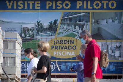 Varias personas caminan junto a un cartel de viviendas en venta en A Mariña (Lugo), el pasado julio.