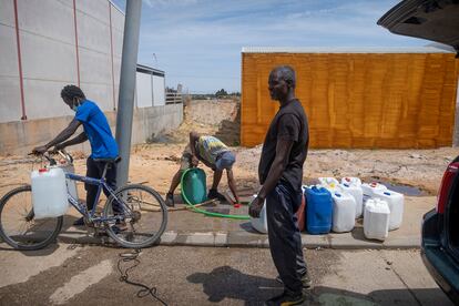 Varios jóvenes llenan garrafas de agua en una toma existente en una de las calles del Polígono Industrial San Jorge, en la localidad onubense de Palos de la Frontera.