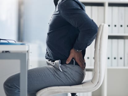Hombre sentado en una silla tocándose la espalda del dolor.