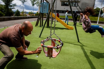 Niños juegan en un parque infantil de Santiago de Compostela, tras su apertura en la nueva normalidad. Un adulto desinfecta un columpio.