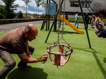 Varios niños juegan en un parque infantil de Santiago tras su reapertura mientras un adulto desinfecta un columpio.