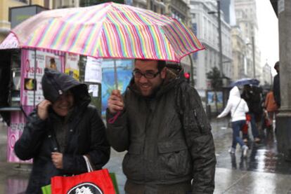 Dos personas ponen buena cara a la lluvia que ayer cayó con fuerza durante buena parte del día en Madrid.