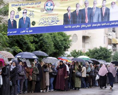 Mujeres hacen cola frente a un colegio electoral, con un pancarta propagandística de la formación de los Hermanos Musulmanes, 'Partido de la Libertad y de la Justicia'.