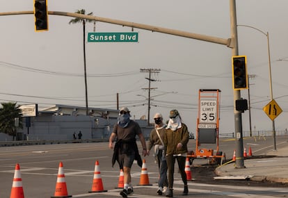 Varios viandantes cruzan, tapados para evitar el humo, entre Sunset y la carretera Pacific Coast Highway, cerradas al tráfico en esa zona a causa de los incendios de Los Ángeles, California.