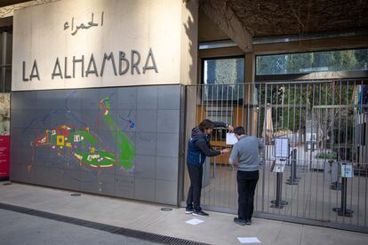 Unos trabajadores colocan un cartel informando del cierre temporal de visitas en la entrada de la Alhambra en Granada.