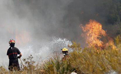Efectivos de bomberos intentan apagar las llamas en la urbanización Cumbres del Sol junto al paraje natural de La Granadella, entre los términos alicantinos de Xàbia y Benitatxell.