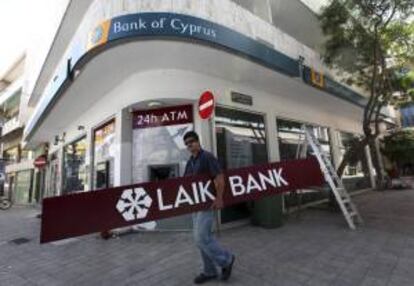 Un hombre cubre la serigrafía del banco Laiki por la del Banco de Chipre en una de sus sucursales en Nicosia (Chipre). EFE/Archivo