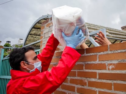 Un voluntario de la Cruz Roja entrega a una mujer un paquete de alimentos y productos de higiene.